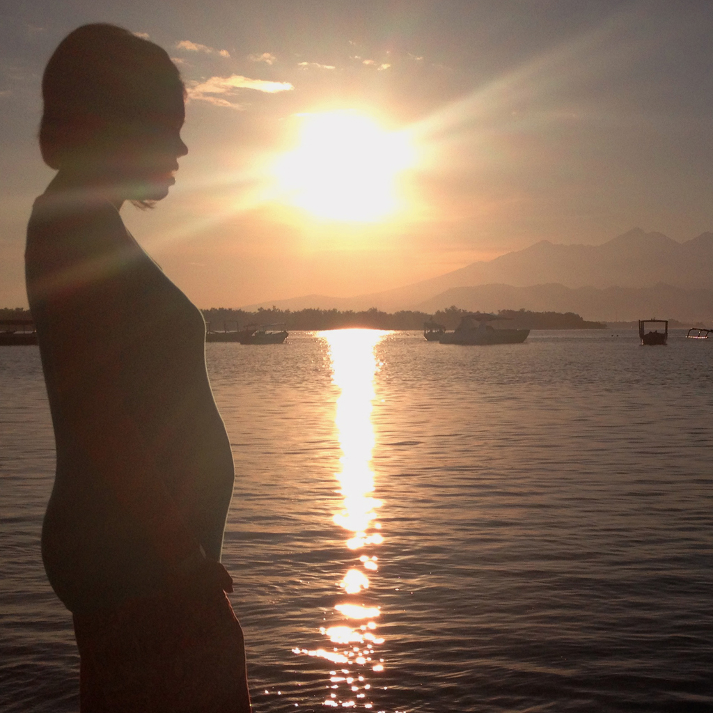 A pregnant woman standing on a beach at sunset